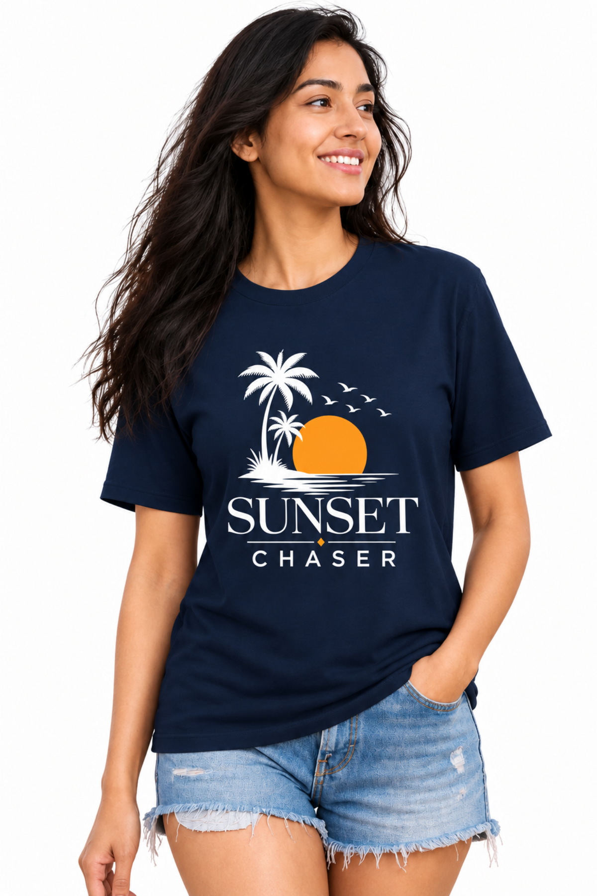 A woman modeling a navy blue t-shirt with a 'Sunset Chaser' graphic print featuring a palm tree, sunset, and birds, paired with denim shorts against a white background.