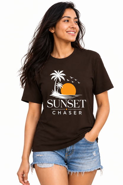 A woman modeling a dark brown t-shirt with a 'Sunset Chaser' graphic print, paired with denim shorts, against a plain white background.