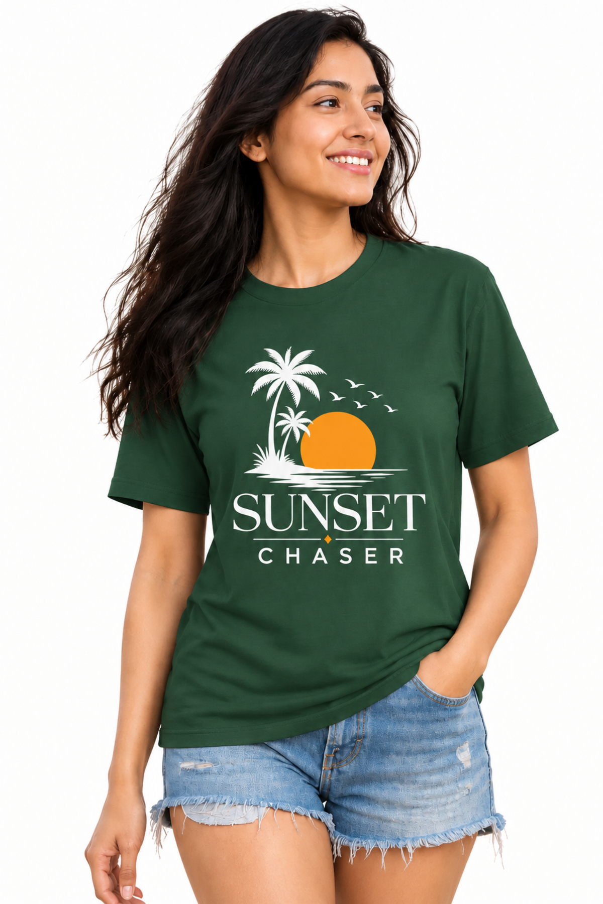 A woman wearing a dark green graphic t-shirt with a palm tree and orange sunset design, paired with denim shorts, against a plain white background.