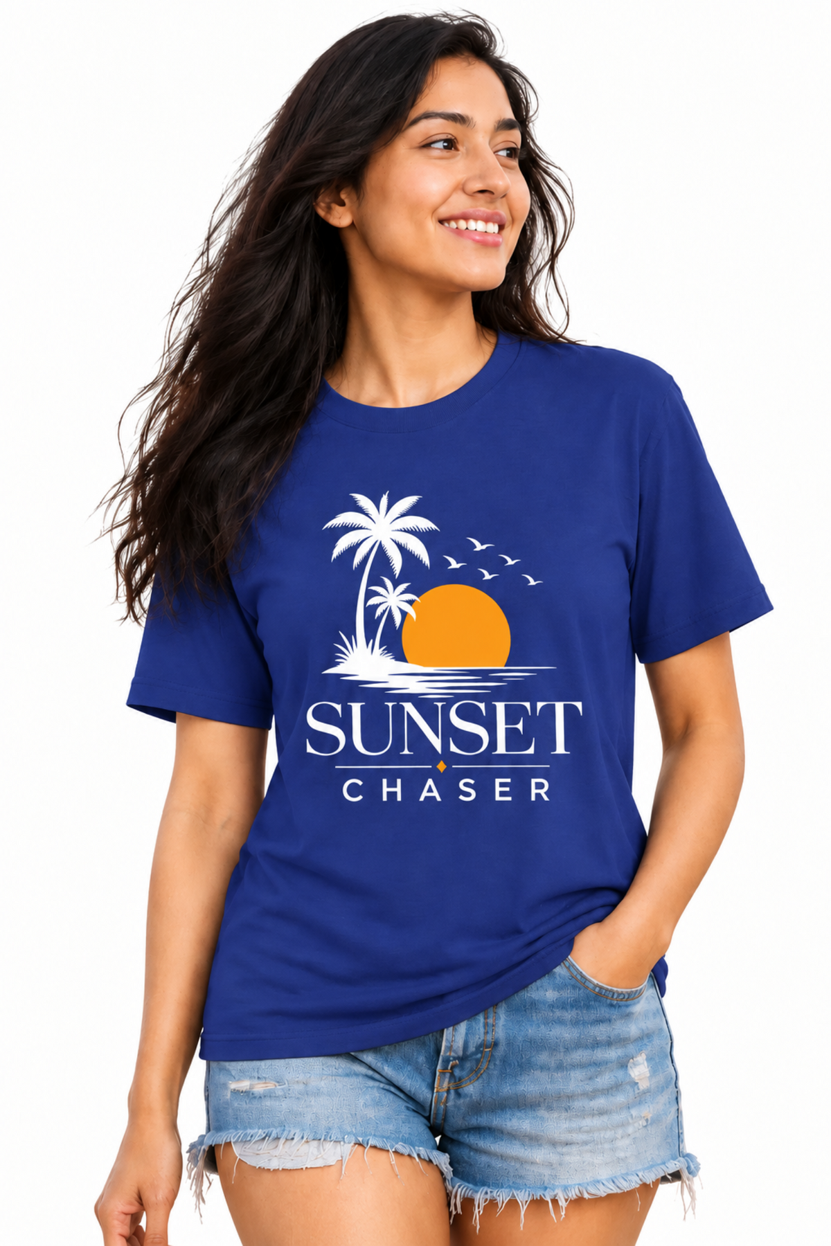 A woman wearing a royal blue crewneck t-shirt with a 'Sunset Chaser' graphic on the front, paired with denim shorts, against a plain white background.