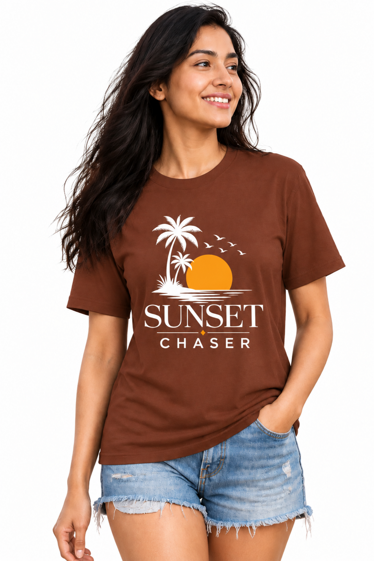 A woman modeling a brown short-sleeve graphic t-shirt with a white palm tree, orange sun, and 'SUNSET CHASER' text, paired with denim shorts against a plain white background.