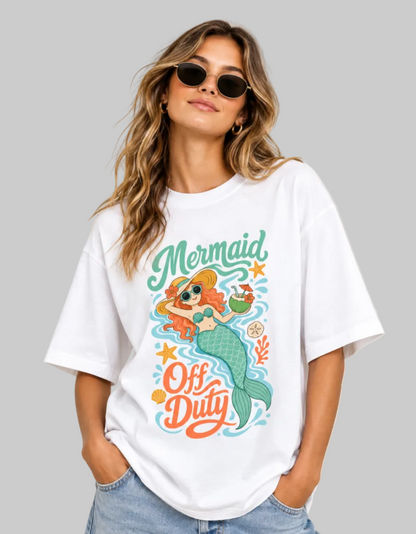 A woman wearing a white oversized graphic t-shirt with a colorful mermaid illustration and the text 'Mermaid Off Duty'.