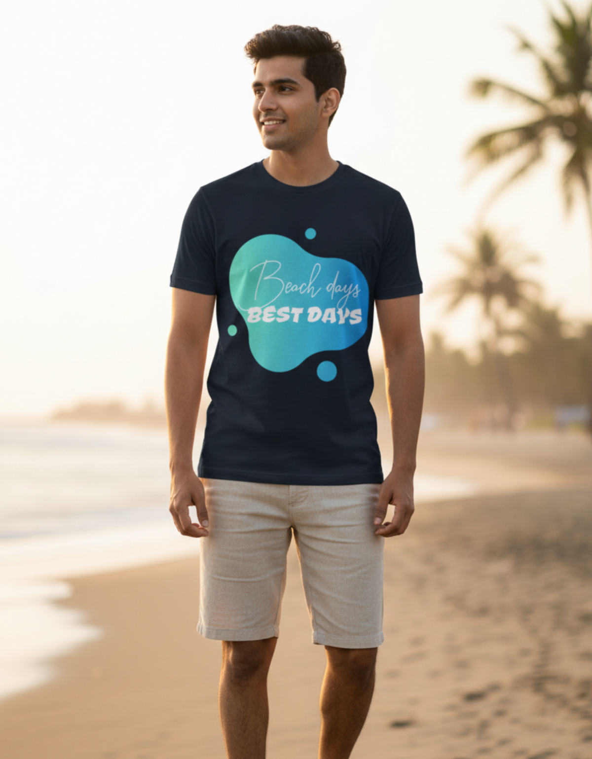 A man standing on a sandy beach wearing a navy blue t-shirt with a teal graphic that reads 'Beach days BEST DAYS' in white script and block letters, paired with beige shorts and white sneakers.