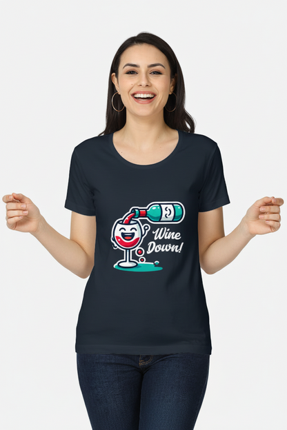 A woman smiling and wearing a dark navy blue t-shirt with a cartoon graphic of a wine glass, a bottle, and the text 'Wine Down!' in white, paired with dark blue jeans, against a light gray background.