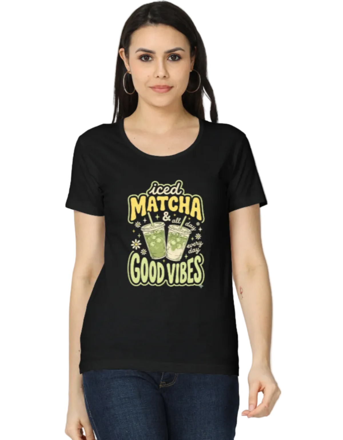 A woman modeling a black short-sleeve t-shirt with a graphic print that reads 'Good MATCHA & tea time GOOD VIBES' in yellow and green lettering, paired with blue jeans against a plain white background.