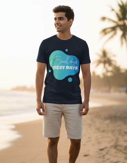 A man standing on a sandy beach wearing a navy blue t-shirt with a teal graphic that reads 'Beach days BEST DAYS' in white script and block letters, paired with beige shorts and white sneakers.