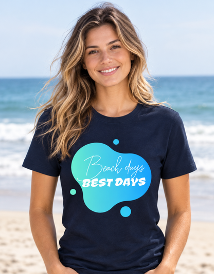 A woman smiling on a beach wearing a navy blue t-shirt with a teal and light blue abstract graphic that reads 'Beach days BEST DAYS'.